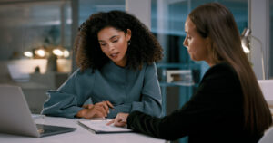 Documents, laptop and business women in meeting at night for proposal, analysis and planning in office. Corporate, collaboration and female workers with in discussion with paperwork, report and data
